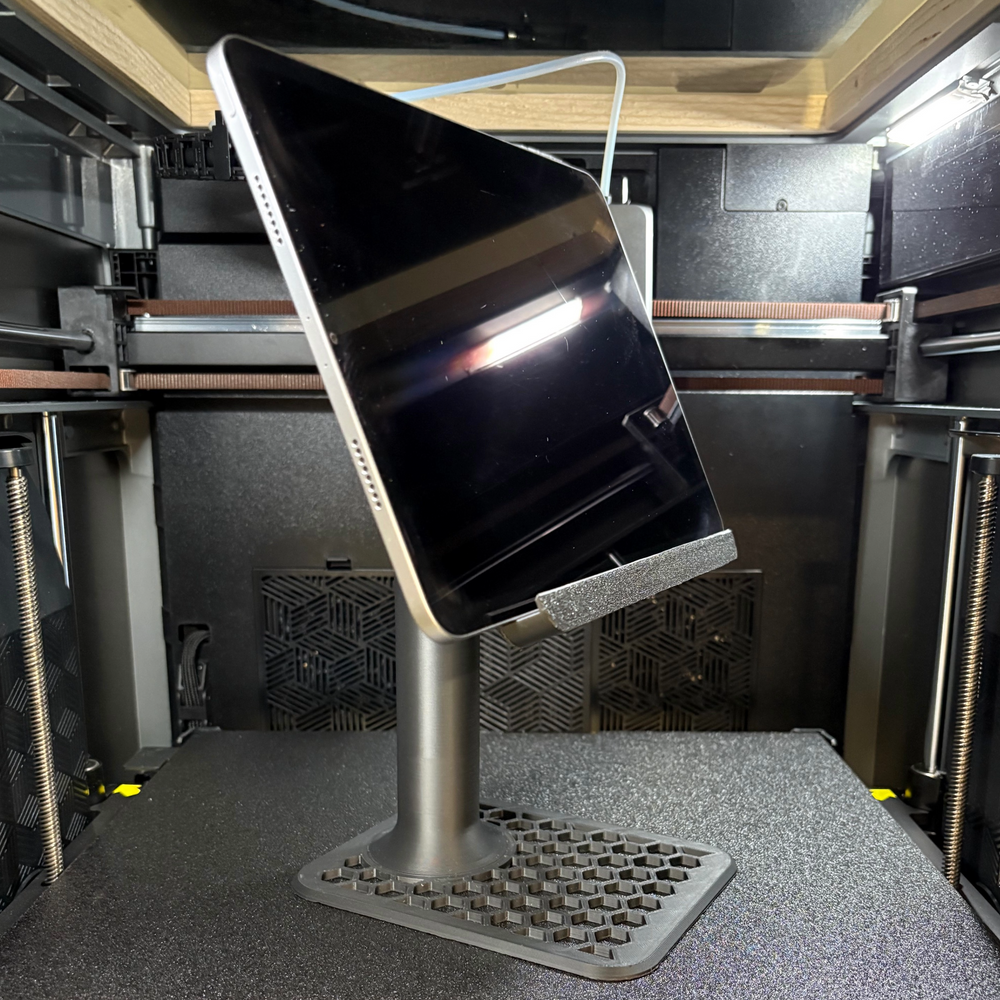 3D printed black adjustable tablet stand holding an iPad on a desktop surface inside a 3D printer enclosure